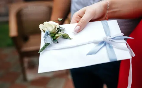 Biała koperta z błękitną wstążką i butonierką, symbolizująca pieniądze z wesela na konto.