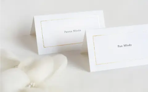 Eleganckie winietki dla pary młodej z subtelną złotą ramką. "Panna Młoda" i "Pan Młody" zapowiadają uroczystość.