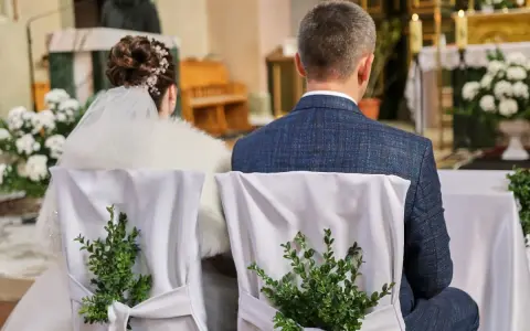 Para młoda siedzi w kościele. Krzesła ozdobione są zielonymi gałązkami. Kto może być świadkiem na ślubie?