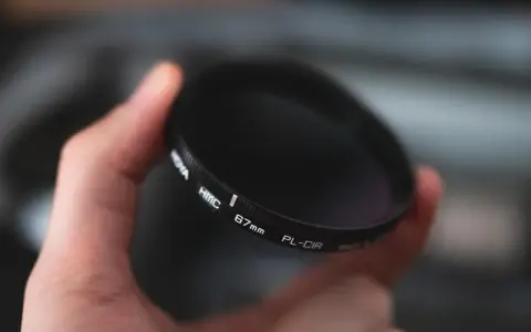 Dłoń trzyma okrągły filtr fotograficzny. To jeden z rodzajów filtrów fotograficznych, który pomaga uzyskać lepsze efekty.