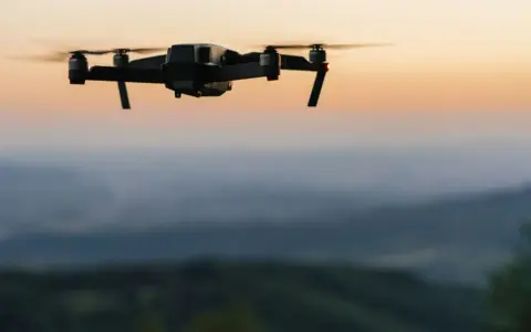 Czarny dron unosi się nad wzgórzami o zachodzie słońca.