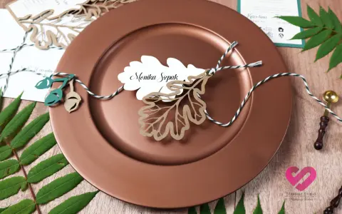 Winietki co to? Eleganckie winietki z imieniem "Monika Szpak" na liściu dębu, ozdobione sznurkiem i żołędziami, na brązowym talerzu.
