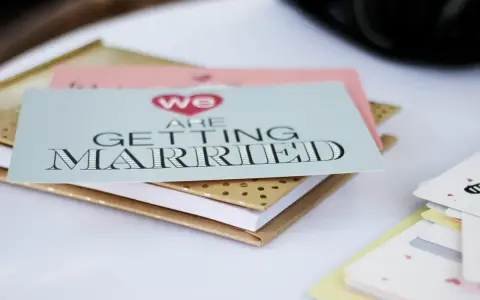 Zaproszenia ślubne "We are getting married" w formacie B0, ułożone na złotym notesie.