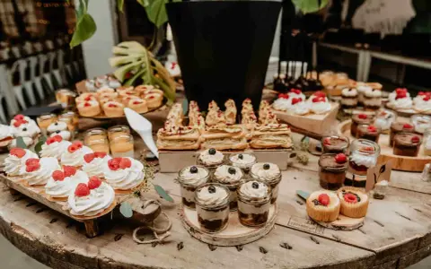 Stół weselny z ciastami na wesele bez kremu: bezy z malinami, mini tarty, deserki w słoiczkach i inne słodkości.
