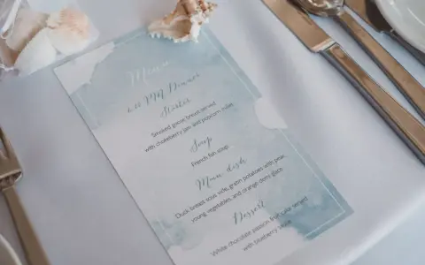 Menu weselne z akwarelowym motywem morskim, ozdobione muszlami.