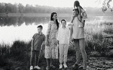 Czarno białe zdjęcie. Rodzina na tle jeziora. Ojciec niesie córkę na barana, obok mama i dwaj synowie.