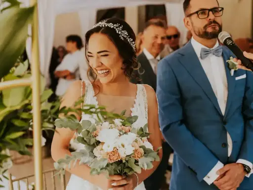 Szczęśliwa panna młoda z bukietem podczas ślubu cywilnego. Pan młody w niebieskim garniturze stoi obok.