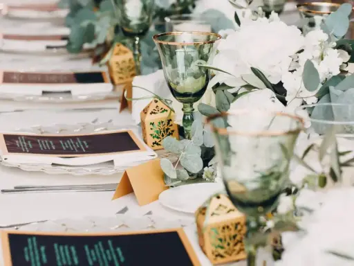 Eleganckie nakrycia stołu na wesele bez alkoholu: zielone kieliszki, menu, ozdobne pudełeczka i bukiety.