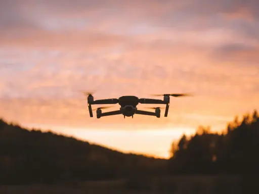 Dron w locie na tle zachodzącego słońca. Jego zasięg pozwala na uchwycenie pięknych krajobrazów.
