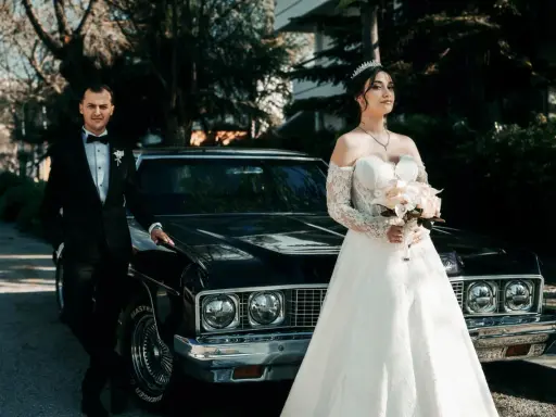 Para, w eleganckim czarnym garniturze, i panna młoda w sukni z koronki, z bukietem w dłoni, stoją obok zabytkowego samochodu. Nawet jeśli nie mam świadków na ślub, ten dzień jest nasz.
