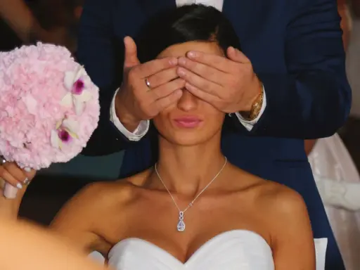 Pan młody zasłania oczy pannie młodej, która trzyma bukiet. To tradycja oczepin, co to za zwyczaj?