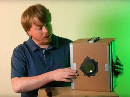 Mężczyzna prezentuje domową camera obscura z kartonu.