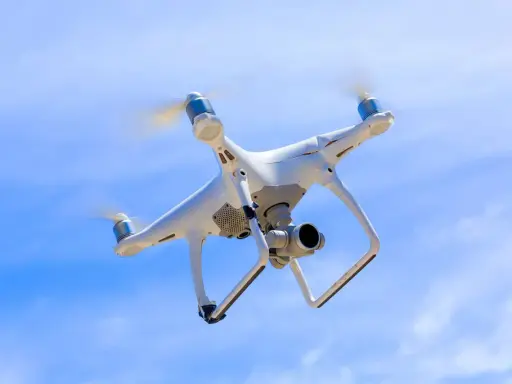 Biały dron z kamerą unosi się na tle błękitnego nieba.