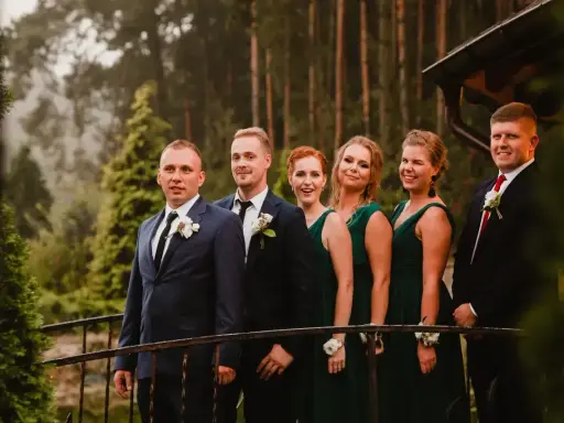 Pan młody i jego drużba, ubrani w garnitury, stoją obok druhen w zielonych sukniach. To idealna drużyna, która wie, co potrzebuje świadek do ślubu kościelnego.