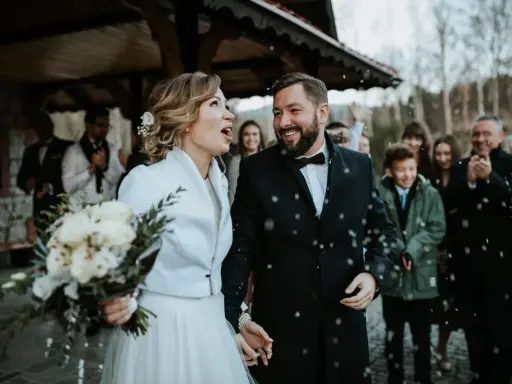 Szczęśliwa para młoda, trzymająca bukiet, wychodzi na zewnątrz podczas swojego ślubu w Adwencie. Sypią się na nich płatki.
