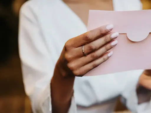 Dłoń z pierścionkiem trzyma różową kopertę. Zastanawiasz się, ile wcześnie zaprasza się na ślub?