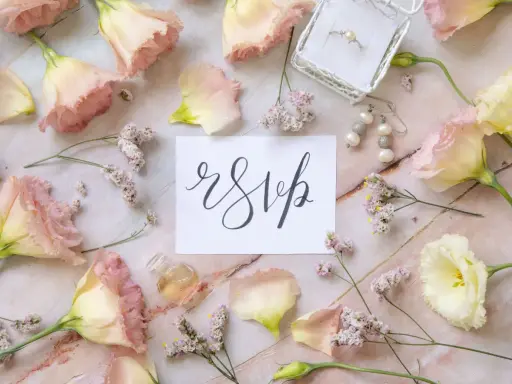 Delikatne kwiaty i biżuteria otaczają kartkę z napisem "rsvp".