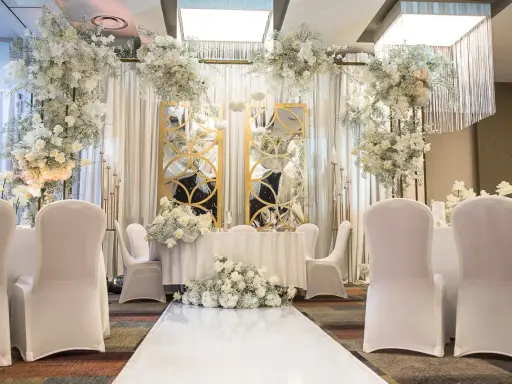 Eleganckie przyjęcie po ślubie cywilnym. Białe kwiaty, złote lustra i białe pokrowce na krzesłach tworzą romantyczną atmosferę.