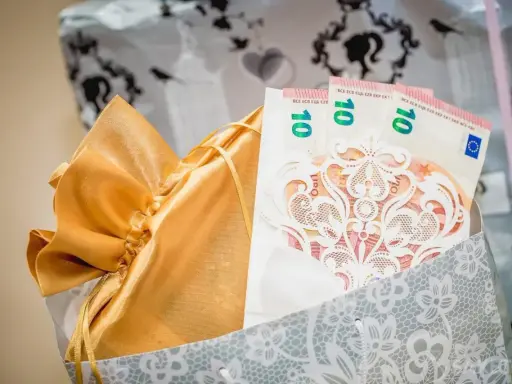 Elegancki sposób na to, jak zapakować pieniądze na ślub: banknoty 10 euro w ozdobnej kopercie, w złotej sakiewce, w ozdobnej torbie.
