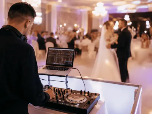 DJ przy konsoli na weselu. Młoda para tańczy na parkiecie. Zastanawiasz się, wesele ile za osobę?