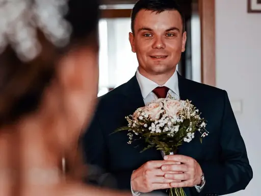 Młody mężczyzna w garniturze trzyma bukiet róż. Czy były ksiądz może wziąć ślub kościelny? To pytanie, które nurtuje wielu.