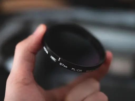 Dłoń trzyma okrągły filtr fotograficzny. To jeden z rodzajów filtrów fotograficznych, który pomaga uzyskać lepsze efekty.
