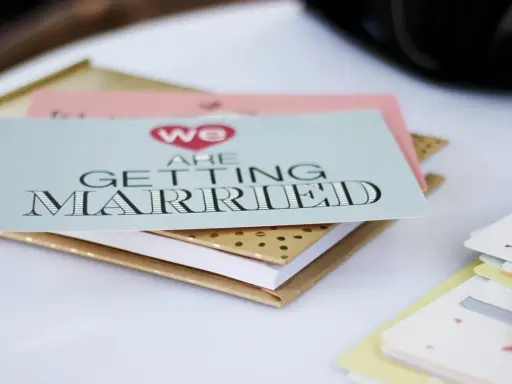Zaproszenia ślubne "We are getting married" w formacie B0, ułożone na złotym notesie.