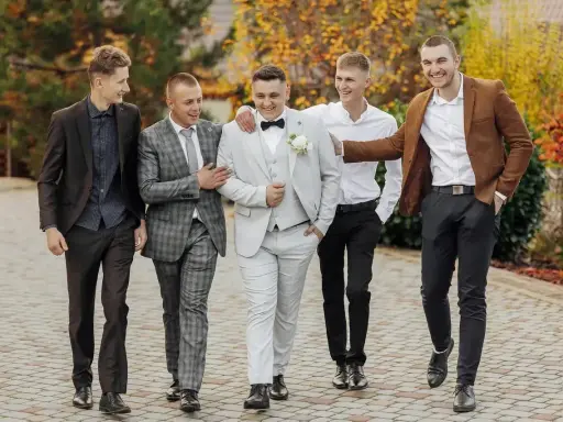 Pięciu panów w garniturach, idealnie dobranych na ślub. Pan młody w jasnym, koledzy w ciemniejszych stylizacjach.
