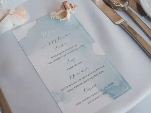 Menu weselne z akwarelowym motywem morskim, ozdobione muszlami.