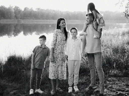 Czarno białe zdjęcie. Rodzina na tle jeziora. Ojciec niesie córkę na barana, obok mama i dwaj synowie.