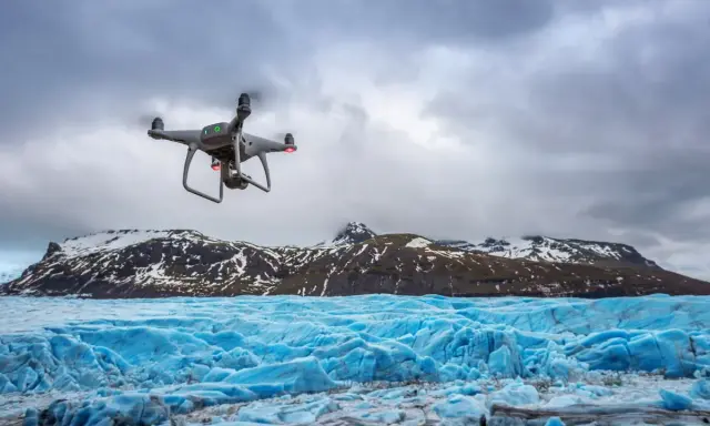 Dron lata nad lodowcem, tworząc niesamowite zdjęcia z drona. W tle góry pokryte śniegiem.