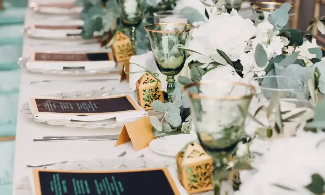 Eleganckie nakrycia stołu na wesele bez alkoholu: zielone kieliszki, menu, ozdobne pudełeczka i bukiety.
