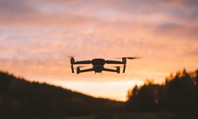 Dron w locie na tle zachodzącego słońca. Jego zasięg pozwala na uchwycenie pięknych krajobrazów.