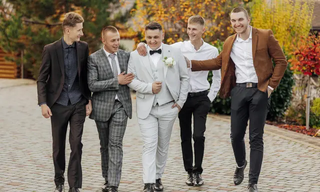 Pięciu mężczyzn w eleganckich strojach, idealnych na wesele. Podpowiedź, jak ubrać się na wesele jako gość mężczyzna.
