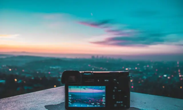 Aparat fotograficzny na tle miejskiego krajobrazu o zachodzie słońca. Różnorodne rodzaje światła tworzą magiczną atmosferę.