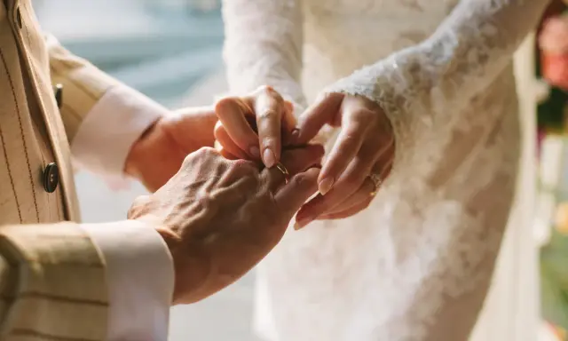 Dłoń pana młodego zakłada obrączkę na palec panny młodej. To piękny moment, jak z piosenki o miłości dla młodej pary.
