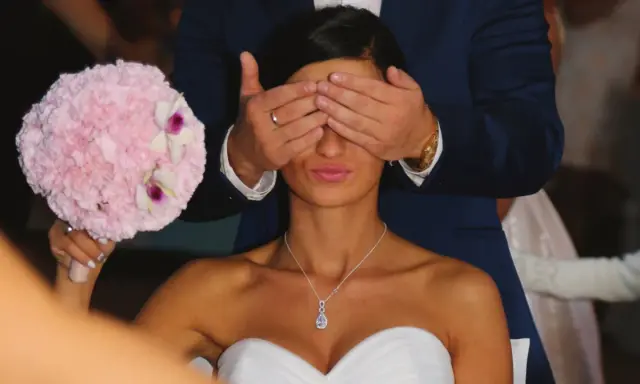 Pan młody zasłania oczy pannie młodej, która trzyma bukiet. To tradycja oczepin, co to za zwyczaj?