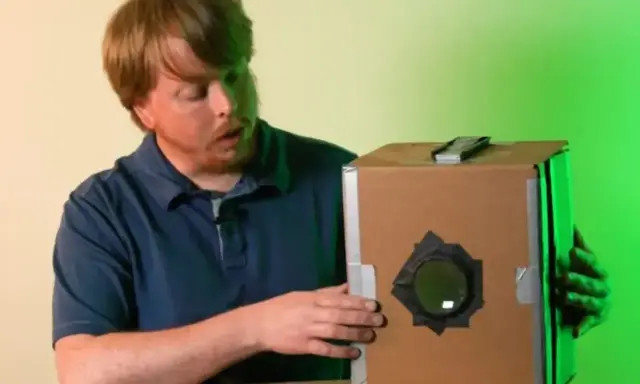 Mężczyzna prezentuje domową camera obscura z kartonu.