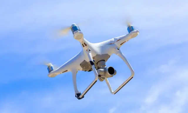 Biały dron z kamerą unosi się na tle błękitnego nieba.