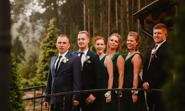 Pan młody i jego drużba, ubrani w garnitury, stoją obok druhen w zielonych sukniach. To idealna drużyna, która wie, co potrzebuje świadek do ślubu kościelnego.