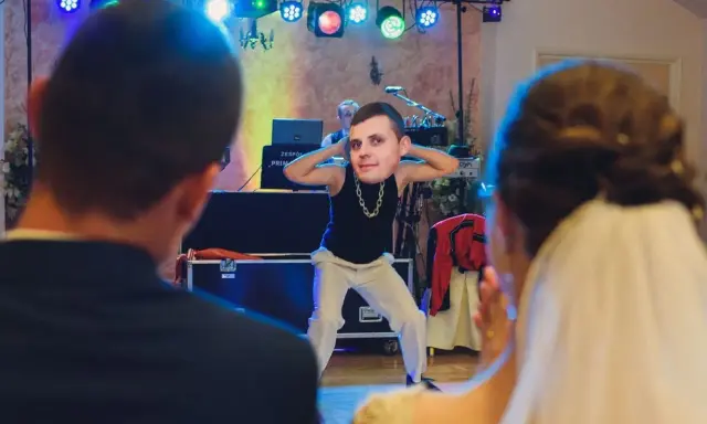 Zabawny pan z twarzą na głowie tańczy na weselu, tworząc nowoczesne zabawy na oczepiny.
