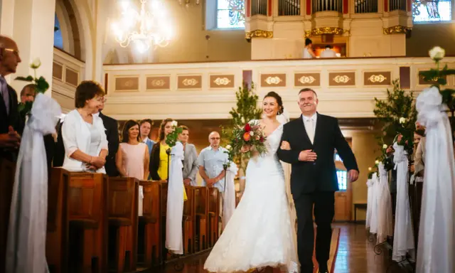 Panna młoda z bukietem idzie do ołtarza z ojcem. Cichy ślub kościelny bez mszy, w kościele pełnym gości.