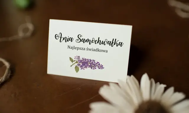 Winietka z napisem "Ania Samochwałka Najlepsza świadkowa" i gałązką bzu. Idealna inspiracja, jak wypisać winietki dla rodziców.