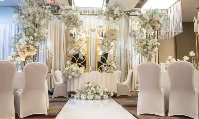 Eleganckie przyjęcie po ślubie cywilnym. Białe kwiaty, złote lustra i białe pokrowce na krzesłach tworzą romantyczną atmosferę.