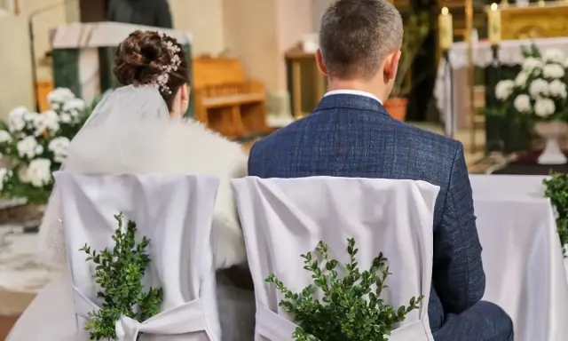 Para młoda siedzi w kościele. Krzesła ozdobione są zielonymi gałązkami. Kto może być świadkiem na ślubie?