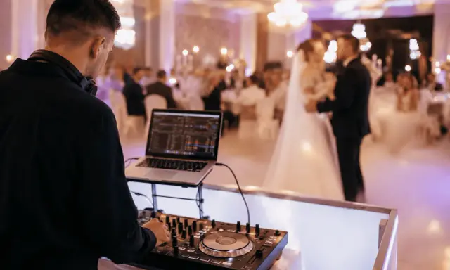 DJ przy konsoli na weselu. Młoda para tańczy na parkiecie. Zastanawiasz się, wesele ile za osobę?