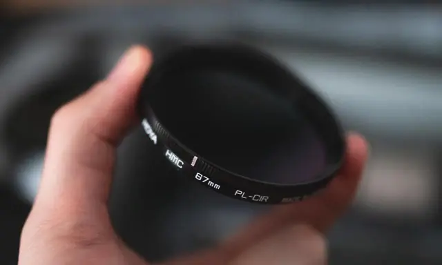 Dłoń trzyma okrągły filtr fotograficzny. To jeden z rodzajów filtrów fotograficznych, który pomaga uzyskać lepsze efekty.