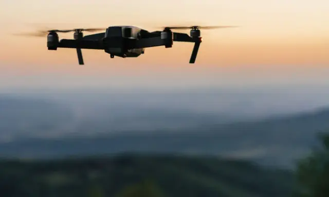 Czarny dron unosi się nad wzgórzami o zachodzie słońca.