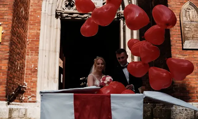Para młoda wychodzi z kościoła w pudełku, otoczona czerwonymi balonami w kształcie serc. Wspaniałe pomysły na wesele niespodzianki!