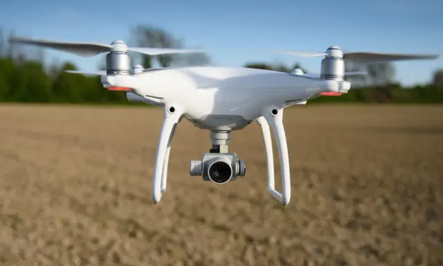 Biały dron DJI Phantom 4 Pro w locie nad polem.
